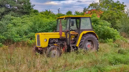old yellow farm tractor standing among greenery, in the countryside