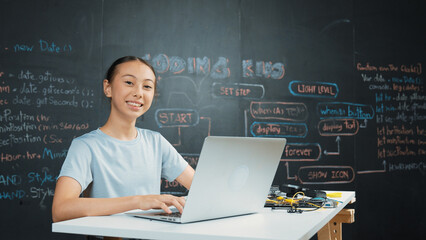 Smart girl programing system by using laptop at blackboard. Highschool student writing engineering code or prompt while looking at camera at STEM technology class. Creative education. Edification.