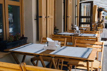 Outdoor empty coffee and restaurant terrace with wooden tables, vintage chairs and linen napkins in Europe. Cafe terrace on the pedestrian street. A set table is waiting for customers.