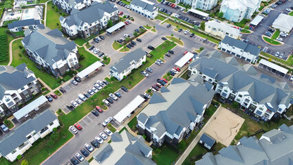 New development suburban farmhouses style apartment complex metal roofing, busy outdoor parking lot in Pflugerville, fast-growing city suburbs of North Austin, Travis County, Texas, aerial view © trongnguyen