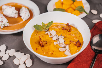 Vegetable soup, pumpkin and carrot puree with seeds, mushrooms, chanterelles and mint in a white bowl on a gray background with a burgundy napkin and a black spoon