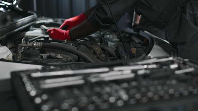 Close-up rack focus shot of tool box in cart in auto repair garage, hands of unrecognizable technicians taking wrenches and removing bolts on engine components during routine checkup