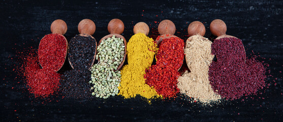 Large collection of spices and herbs in wooden spoons. Seasonings for food isolated on a black...