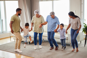 Family, dance and bonding in living room while holding hands for fun, support or people playing game. Grandparents, parents and children in home for birthday party, celebration and freedom with music