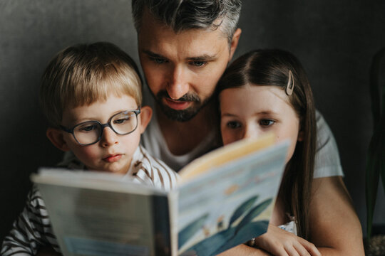 Father reading book with son and daughter at home