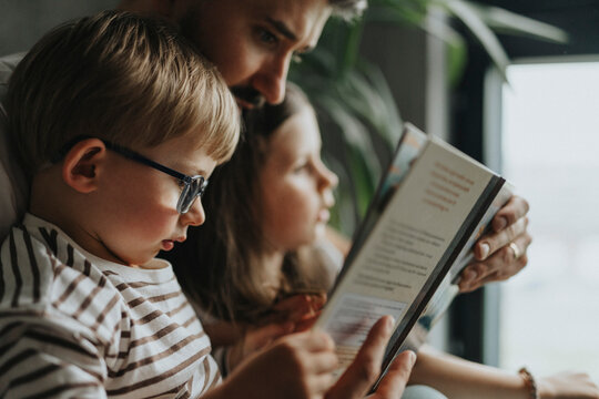 Focused boy reading book with father and sister at home