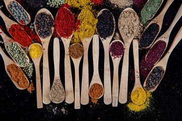 Large collection of spices and herbs in wooden spoons. Seasonings for food isolated on a black...