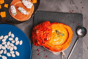 Baked pumpkin stuffed with mashed vegetables with chanterelle mushrooms on a black board and a blue plate with pumpkin seeds