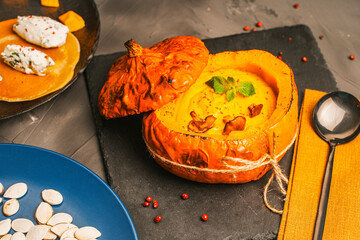 Baked pumpkin stuffed with mashed vegetables with chanterelle mushrooms on a black board and a blue plate with pumpkin seeds