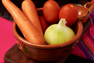 Basic vegetables such as carrots, tomatoes and an onion placed in a clay pot, everything is placed...
