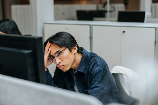 Exhausted male entrepreneur with head in hand looking at computer screen in office