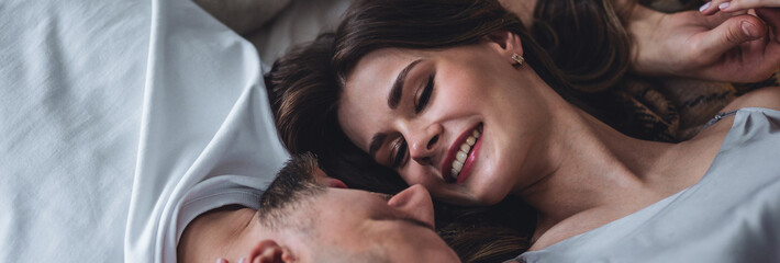 Banner relationships. Beautiful happy loving young couple relaxing in bed, looking at each other. Cozy home atmosphere, tenderness, closeness. Embracing, kissing. Lazy weekend, slow living concept