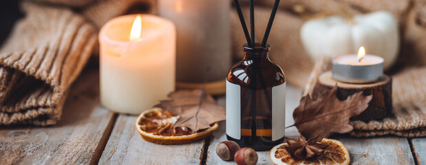 Hello autumn, cozy slow living. Pumpkin, aromatic candle, warm sweaters, dry fall leaves, cinnamon, anise in golden lights with bokeh on white wooden background. Thanksgiving apartment decor banner