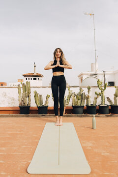 Young woman practicing prayer pose while standing on yoga mat