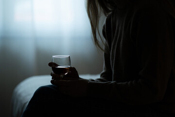 Depressed, divorced woman sitting alone at home and drinking a glass of red wine because of problems at work and troubles in relationships. 
