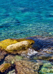 Coastal landscape with stone beach and salt water with algae in the Mediterranean Sea in summer.