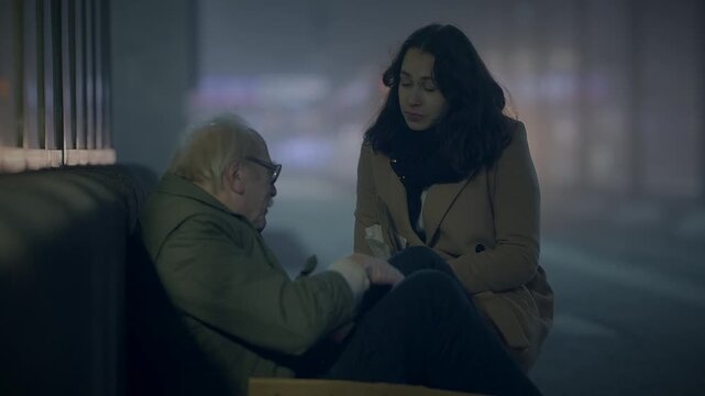 In the darkness of the city, a woman is seen comforting an elderly man on the nighttime street