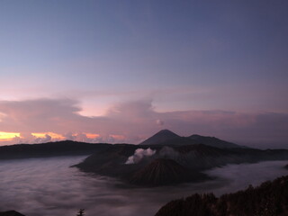 Fototapeta premium Panoramic landscape view of Mount Bromo volcano in Indonesia, surrounded by smoke and fog. The iconic volcano stands tall amidst a dramatic setting, with misty fogs enhancing the mystical atmosphere. 