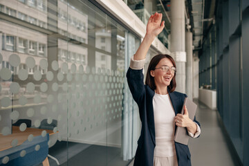 A businesswoman waves in a modern office, showing professionalism and positivity