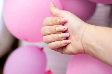 female hand with yellow and pink nails on pink background