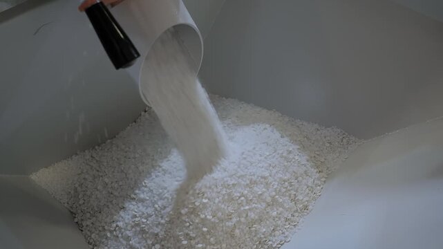 Plastic pelletizer recycling machine: white recycled plastic granules, pellets are falling into metal container - final stage: collecting, close up view. Reuse, waste reduction and sustainable concept
