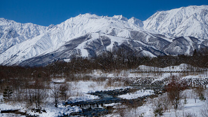 Fototapeta premium 冬の北アルプスと雪が残る河川 長野県白馬村