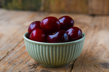 Ripe cherries in a ceramic green bowl on a wooden background. Minimalism.