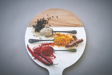 Board, spices and spoon in gray background for flavor, aroma and sensory appeal for creativity with culinary. Studio, condiment and seasoning for cooking with curry, powder and ingredients collection