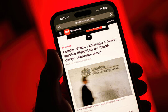 Paris, France - Jul 20, 2024: From a point-of-view perspective, a male hand holds an iPhone displaying a CNN Business article about the London Stock Exchange's news service disruption