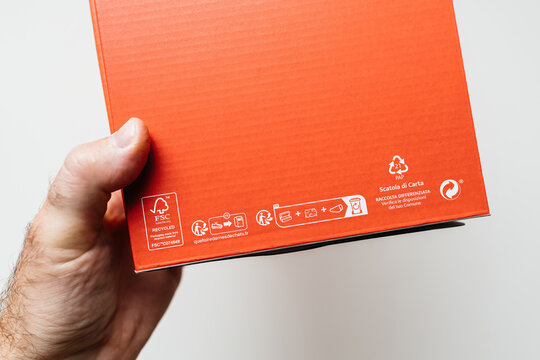 Paris, France - May 29, 2024: A hand holds an orange cardboard box, focusing on its recycling and FSC certification symbols. The box's surface includes instructions for proper disposal 