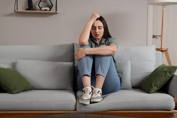 Depressed young woman sitting on sofa at home