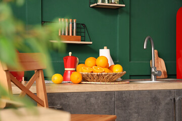 Wicker plate with citruses on counter in stylish green kitchen