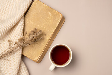Vintage book, scarf and cup tea on beige background. Leisure concept, reading a book. Flat lay, top view