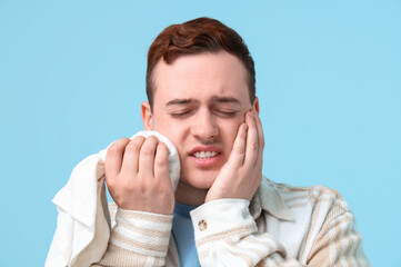 Young man with cold compress suffering from toothache on blue background