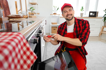 Male technician with screwdriver repairing oven in kitchen