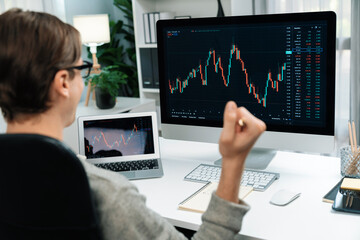 Smart business trader in casual day successful wealth with raising fist up highest profit value of dynamic increased stock market graph profitable on pc and tablet screen at modern office. Pecuniary.
