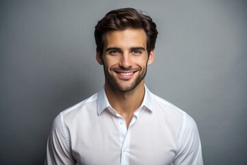 Obraz premium Handsome young man in white shirt smiling and looking at camera while standing against grey background