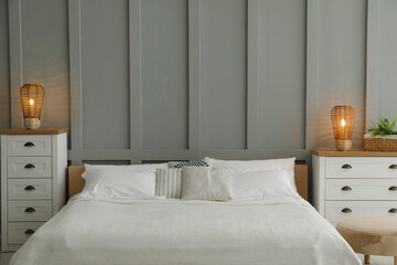 Stylish bedroom interior with comfortable bed, lamps and houseplant