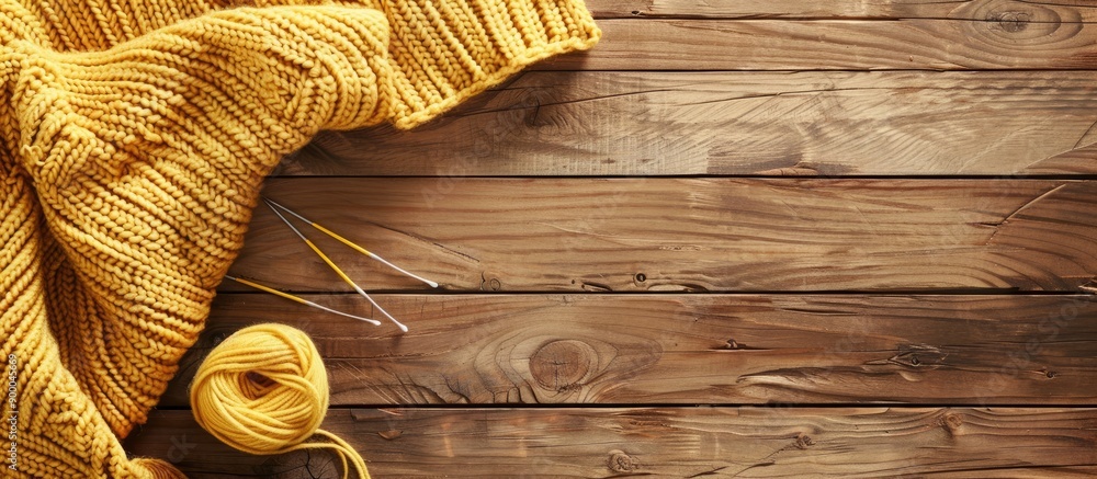 Poster top view of light yellow knitting wool needles knitted fabric and yarn on a wooden surface with copy