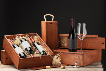 Boxes with wine bottles and glass on wooden table against black background