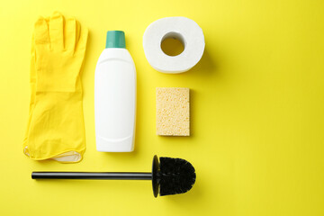 Toilet brush, paper roll, bottle of cleaning product, sponge and gloves on yellow background, flat lay. Space for text