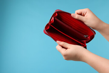 Woman with empty wallet on light blue background, closeup