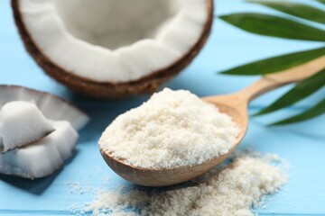 Fresh coconut flour in spoon, nut and palm leaf on light blue wooden table, closeup