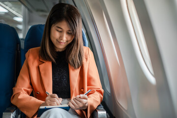 Fototapeta premium A young woman in a business casual outfit writing in a notebook while seated on an airplane, showcasing productivity during travel.