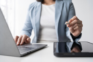 Businesswoman is using laptop computer and holding stylus pen for graphics tablet while working at...