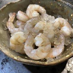 A bowl of fresh, raw shrimp on ice. The shrimp are pink and white, and they are arranged in a haphazard way in the bowl. The bowl is sitting on a dark surface.