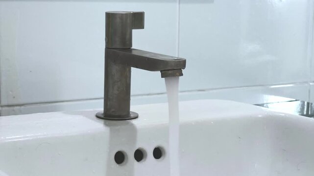 turn valve and shut off water pouring from faucet to bathroom sink, slow motion shot.