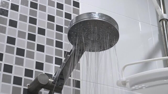 Shower head, flowing water in bathroom. Bottom view of holes in shower head built into. Water flows pouring down from shower head. Using water, taking bath, douche, showering