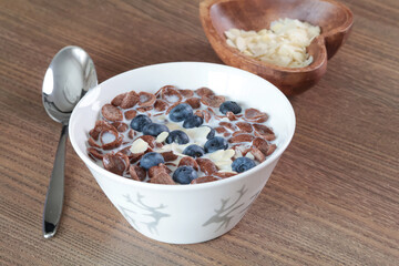 Chocolate cornflakes with blueberries in milk. Ceramic food bowl. Almond nut flakes for healthy eating. 