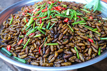 Closeup of a plate of fried crickets with chili peppers and spring onions. A popular street food in many parts of Asia. Fried Crickets with Chili and Spring Onions Background.